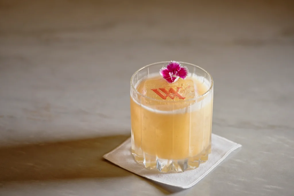 Exquisite cocktail garnished with a flower and the Waldorf Astoria Cancun logo, a perfect blend of elegance and flavor
