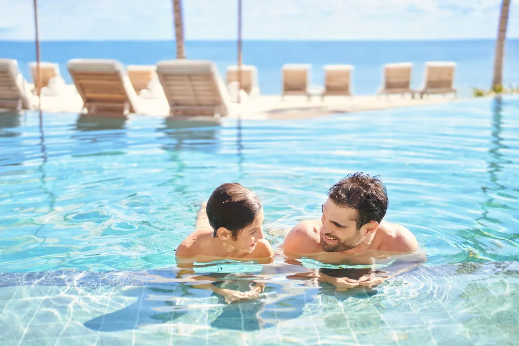 A father and his child enjoying a joyful moment in the sparkling pool of the Waldorf Astoria Cancun, surrounded by luxury and relaxation.