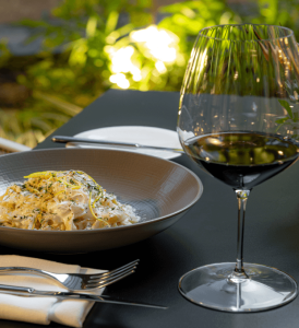 A plate of pasta served with a glass of red wine at Chaya restaurant in Waldorf Astoria, creating a delicious and elegant dining experience.