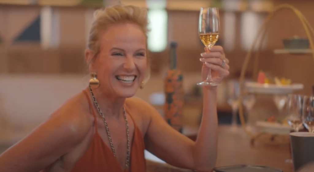 A joyful woman holding a glass of champagne, smiling radiantly as she enjoys a moment of celebration and elegance.