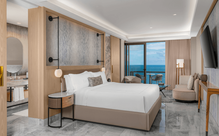 A luxurious hotel room at Waldorf Astoria featuring a king-size bed, a TV, and stunning ocean views.