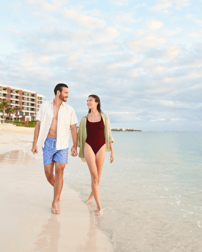 Una pareja paseando por la playa del Waldorf Astoria Cancún, con el océano al fondo y el hotel a la vista, creando una atmósfera serena y romántica.