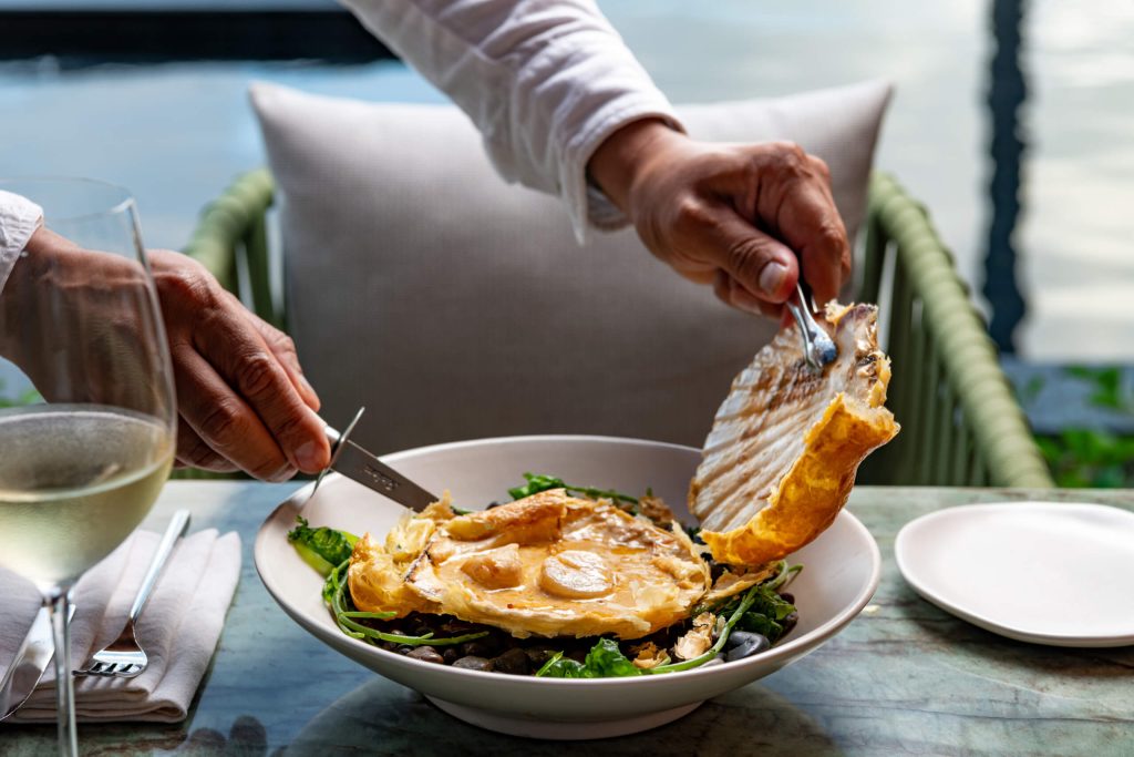 A waiter at Waldorf Astoria Cancun serving a delicious plate of scallops with a refreshing glass of white wine at the elegant Malpeque restaurant.