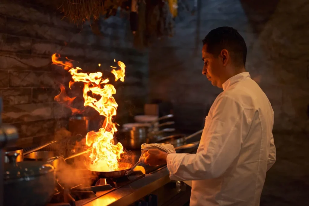 A chef at Malpeque restaurant cooking live with a large flame, showcasing culinary skill and excitement in the kitchen.