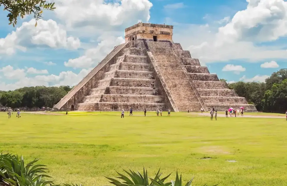 The ruins of Chichen Itza surrounded by lush vegetation, showcasing ancient architecture amidst a natural, green landscape.