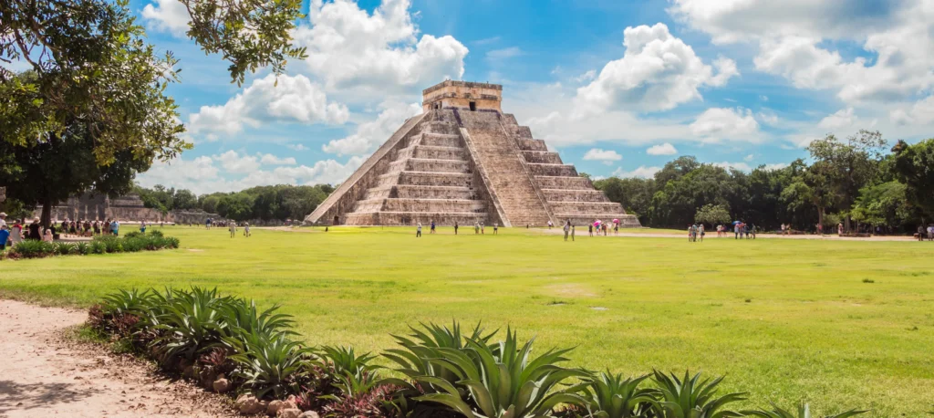 The ruins of Chichen Itza surrounded by lush vegetation, showcasing ancient architecture amidst a natural, green landscape.