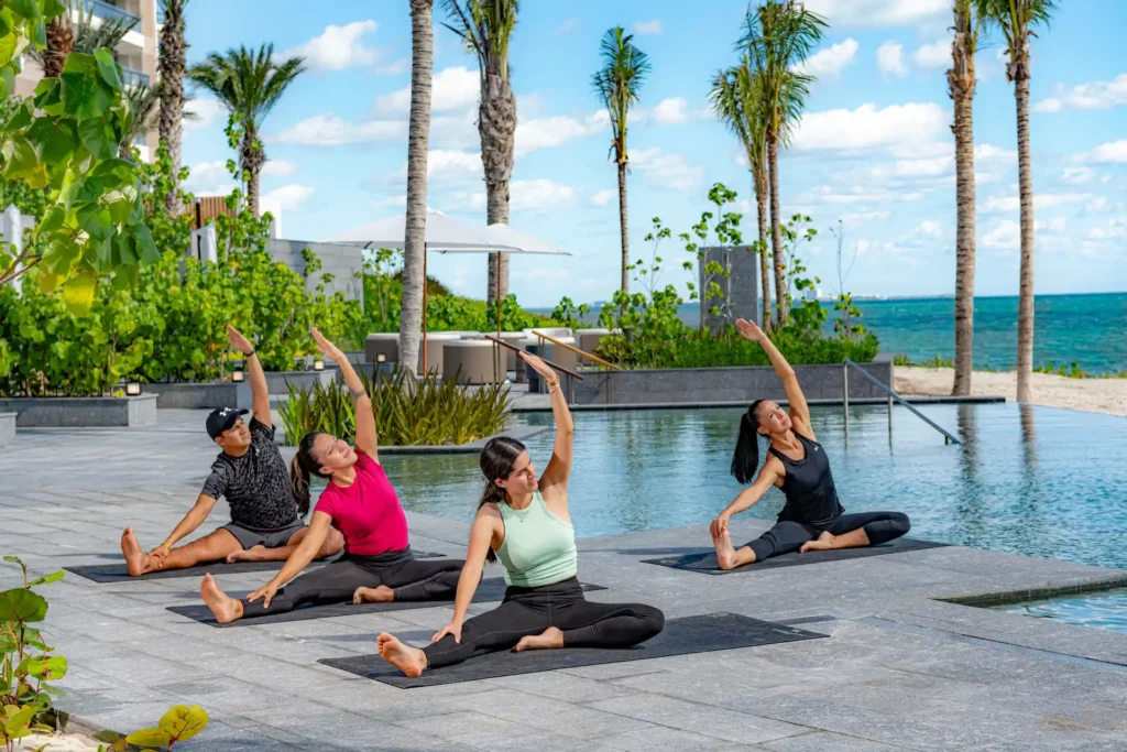 Un grupo de mujeres practicando yoga junto a la piscina del Waldorf Astoria Cancún, rodeadas de un ambiente sereno y tranquilo.