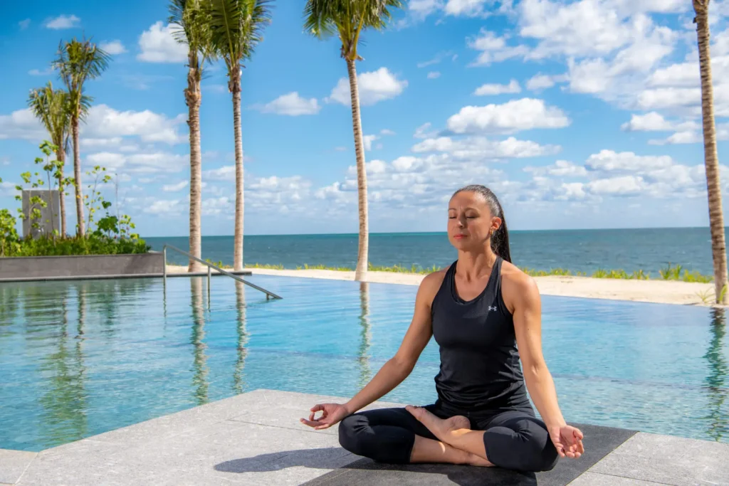 A woman practicing yoga at the edge of the pool, with the ocean in the background, creating a peaceful and serene atmosphere.